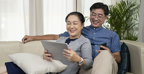 una pareja asiática sonríe y mira la computadora en el sofá