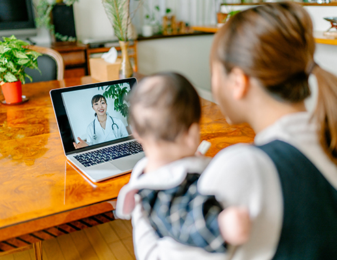 Una madre con su bebé llama por video a un médico mediante una computadora portátil desde su casa.