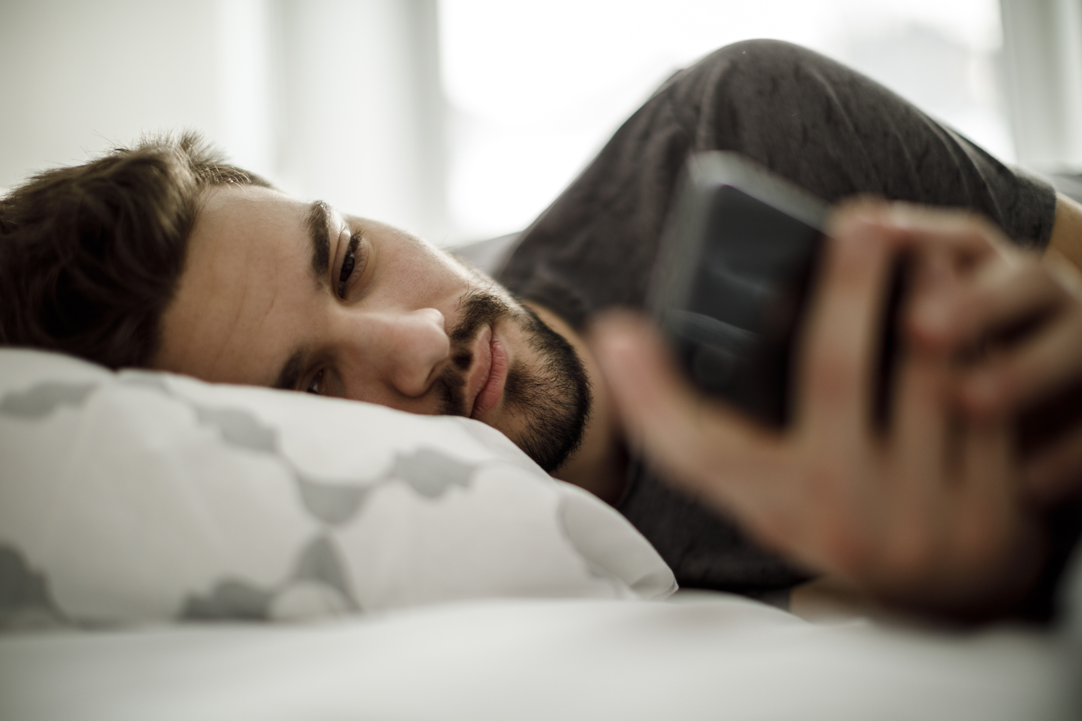 Hombre con expresión triste en cama enviando un mensaje de texto