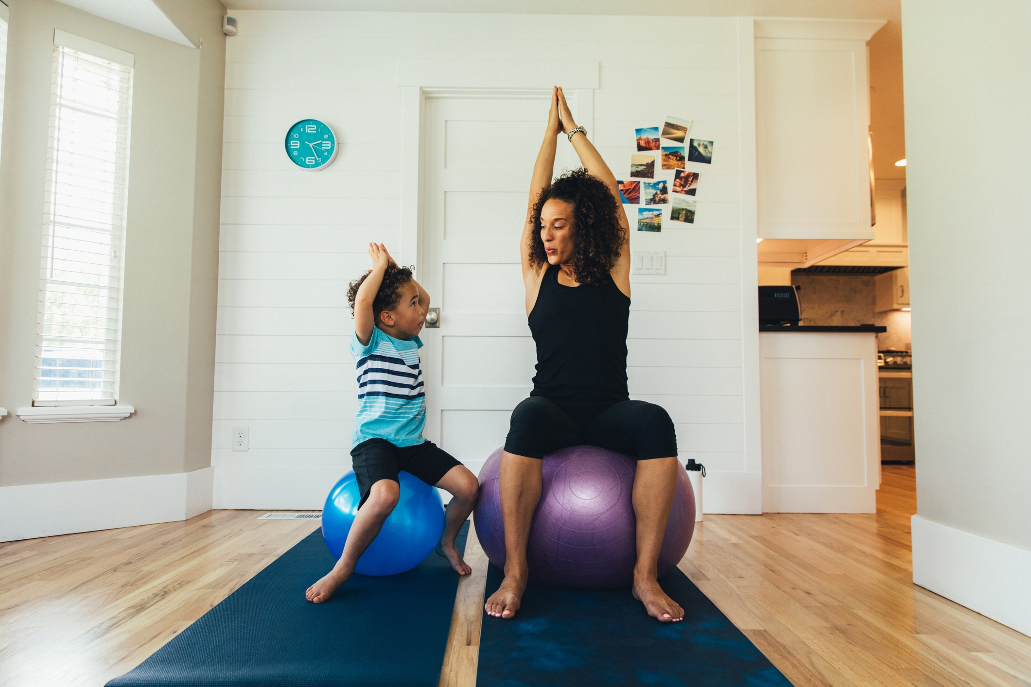 Una madre hace ejercicio sobre una pelota de gimnasio con su hijo pequeño dentro de su casa. Ella enseña al niño la importancia de un estilo de vida saludable a través de estiramientos y ejercicios apropiados.