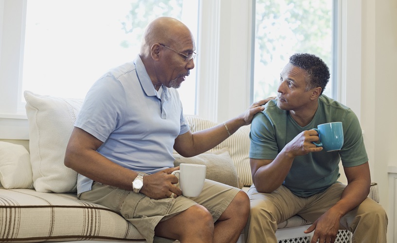 Padre e hijo mayor conversando mientras toman café en el sofá.