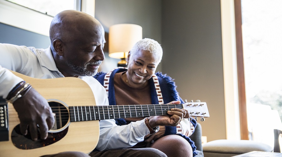 Hombre adulto mayor tocando una guitarra acústica para su esposa en casa