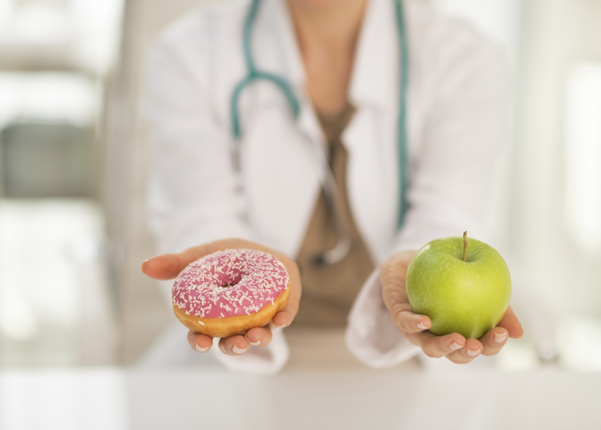 Primer plano sobre un médico dando a elegir entre manzana y dónut