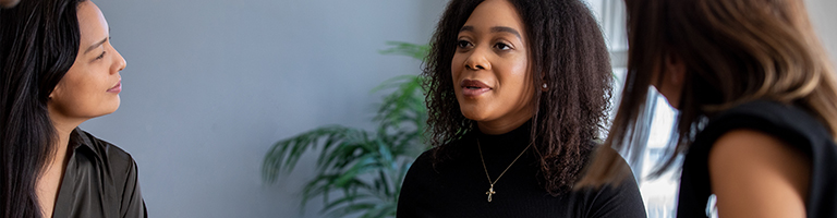 Young woman talks to diverse group of adults during group therapy meeting