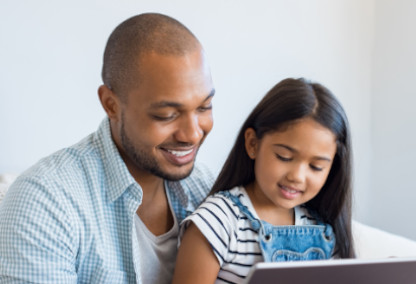 Padre joven e hija sonriendo y mirando una tableta