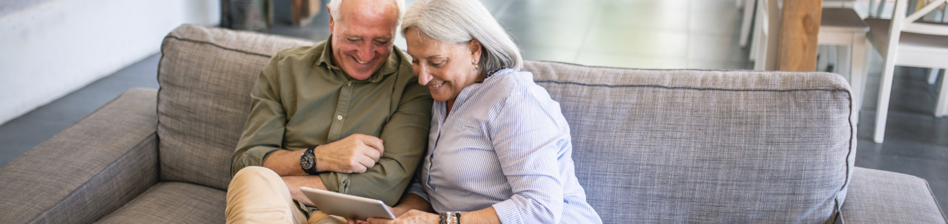 Pareja de adultos mayores sonriendo y mirando un dispositivo de tableta